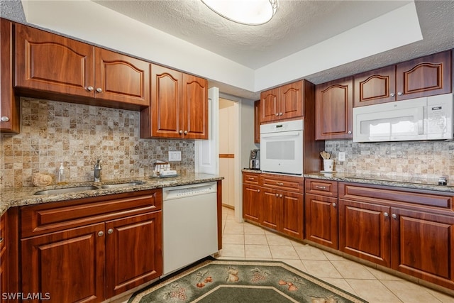 kitchen with backsplash, white appliances, a textured ceiling, sink, and light tile floors