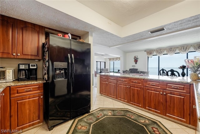 kitchen featuring a textured ceiling, light tile flooring, black fridge with ice dispenser, and light stone countertops