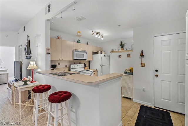 kitchen with a kitchen breakfast bar, white appliances, kitchen peninsula, tasteful backsplash, and track lighting