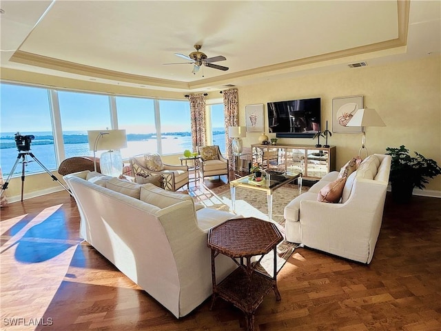 living room featuring ornamental molding, a tray ceiling, ceiling fan, dark wood-type flooring, and a water view