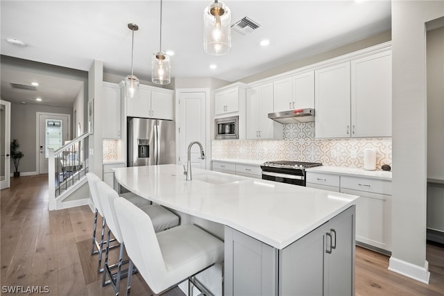 kitchen featuring backsplash, appliances with stainless steel finishes, a kitchen island with sink, and light hardwood / wood-style flooring