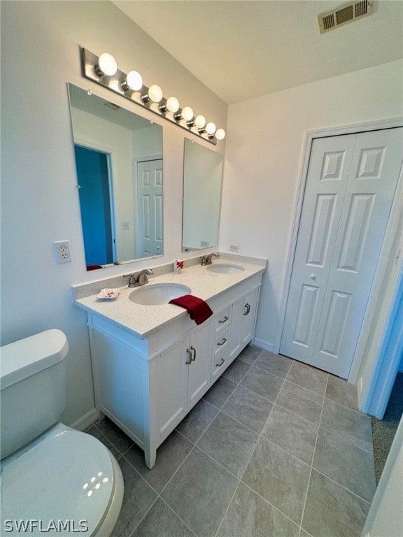 bathroom featuring vanity with extensive cabinet space, tile floors, toilet, and double sink