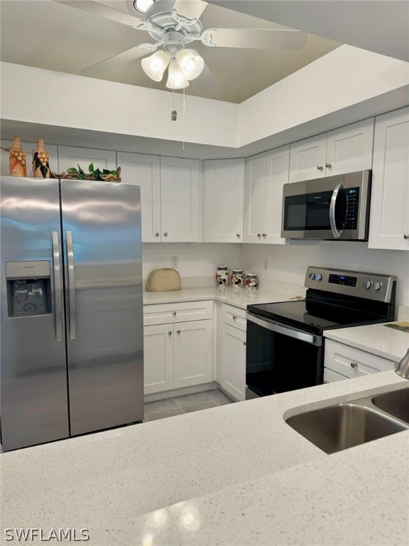 kitchen with white cabinets, light stone countertops, stainless steel appliances, sink, and ceiling fan