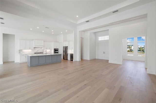 unfurnished living room with a high ceiling, sink, and light hardwood / wood-style flooring