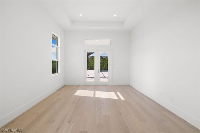 spare room featuring french doors, a raised ceiling, and light wood-type flooring