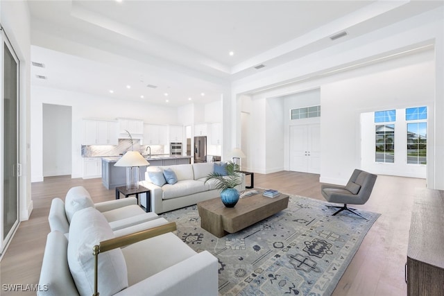 living room with a tray ceiling, sink, a high ceiling, and light wood-type flooring