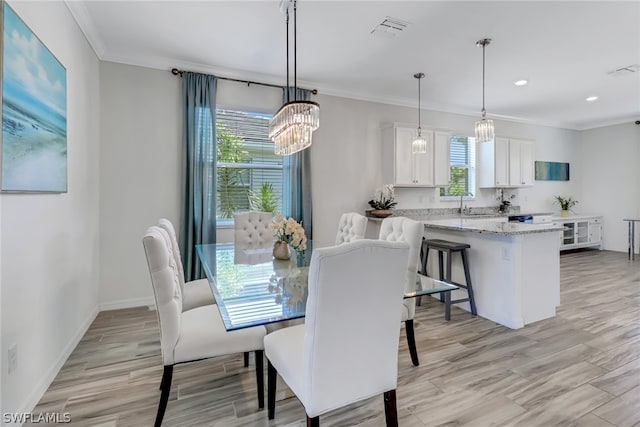 dining space featuring sink, light hardwood / wood-style flooring, crown molding, and an inviting chandelier