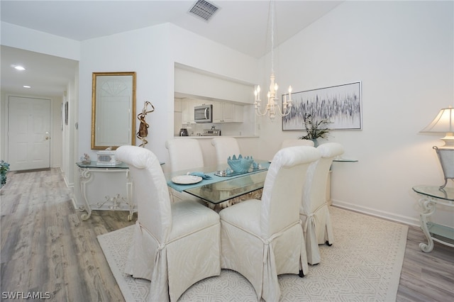 dining area with vaulted ceiling, light hardwood / wood-style floors, and an inviting chandelier