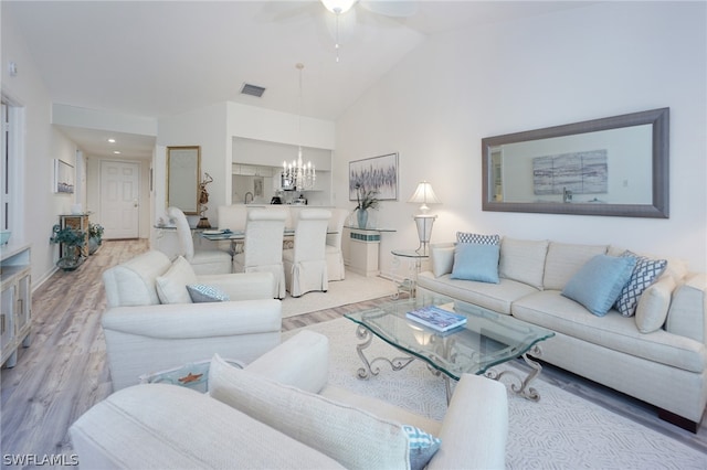 living room with ceiling fan with notable chandelier, light hardwood / wood-style floors, and vaulted ceiling