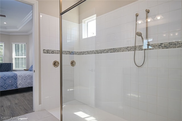 bathroom with a tray ceiling, crown molding, wood-type flooring, and tiled shower