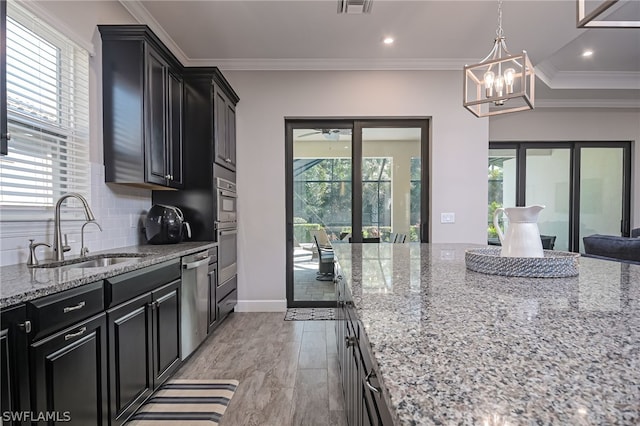 kitchen featuring sink, crown molding, stainless steel appliances, light stone countertops, and decorative light fixtures