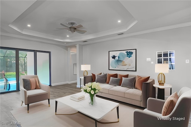 living room featuring a raised ceiling, ornamental molding, ceiling fan, and light wood-type flooring