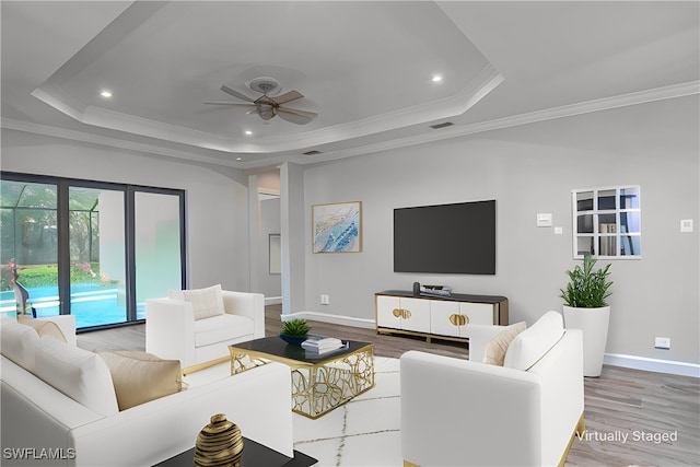 living room with a tray ceiling, light hardwood / wood-style flooring, ornamental molding, and ceiling fan