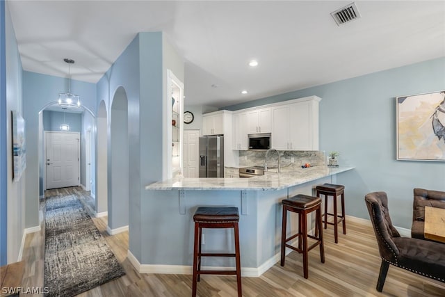 kitchen with appliances with stainless steel finishes, light hardwood / wood-style flooring, hanging light fixtures, tasteful backsplash, and a breakfast bar