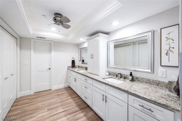 bathroom with ceiling fan, double vanity, a tray ceiling, hardwood / wood-style floors, and ornamental molding