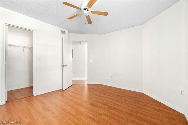 unfurnished bedroom featuring a walk in closet, ceiling fan, a textured ceiling, light hardwood / wood-style floors, and a closet