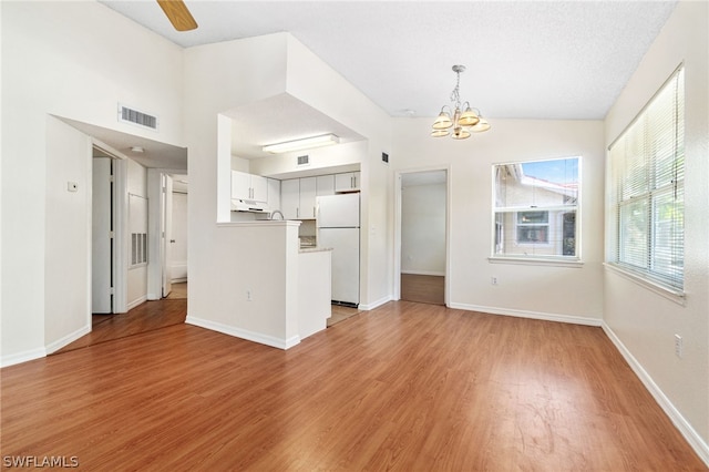 unfurnished living room with a textured ceiling, vaulted ceiling, ceiling fan with notable chandelier, and light wood-type flooring