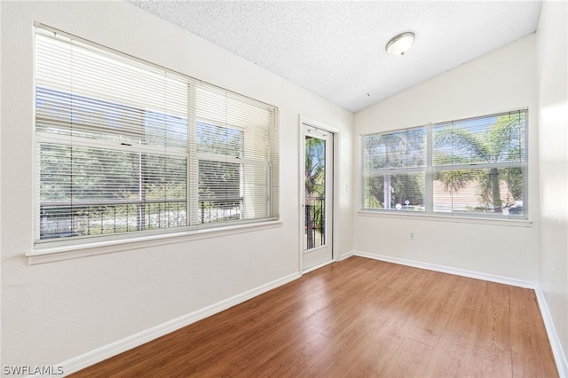 spare room featuring a textured ceiling, hardwood / wood-style flooring, and lofted ceiling