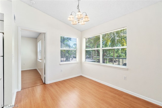 spare room with a textured ceiling, lofted ceiling, a notable chandelier, and hardwood / wood-style flooring