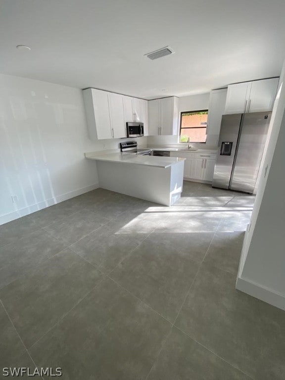 kitchen with kitchen peninsula, appliances with stainless steel finishes, white cabinetry, and light tile floors