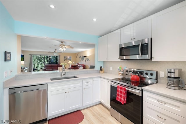 kitchen with appliances with stainless steel finishes, light wood-type flooring, ceiling fan, sink, and white cabinets