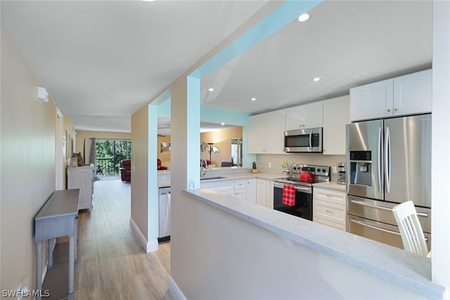 kitchen with light stone counters, white cabinets, stainless steel appliances, and light wood-type flooring