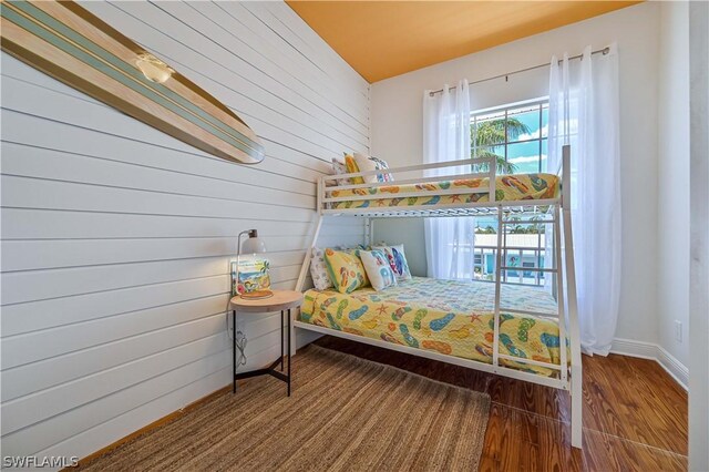 bedroom with wood walls, wood-type flooring, and lofted ceiling