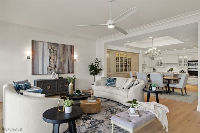 living room featuring light wood finished floors, recessed lighting, a raised ceiling, and crown molding