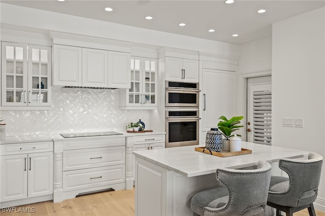 kitchen featuring a breakfast bar area, light wood-style flooring, double oven, white cabinets, and black electric cooktop