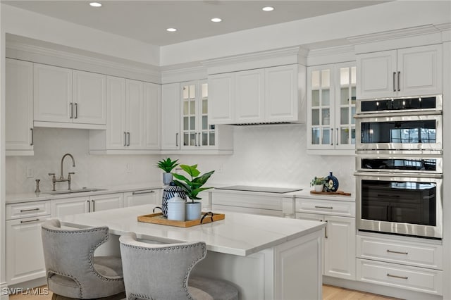 kitchen featuring stainless steel double oven, white cabinets, a sink, and black electric cooktop