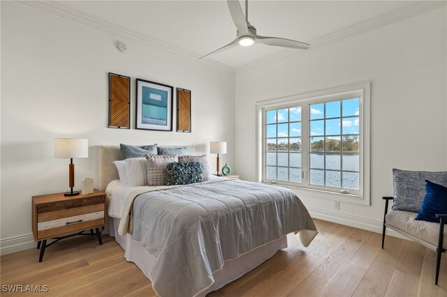 bedroom with crown molding, a water view, light wood-style floors, ceiling fan, and baseboards