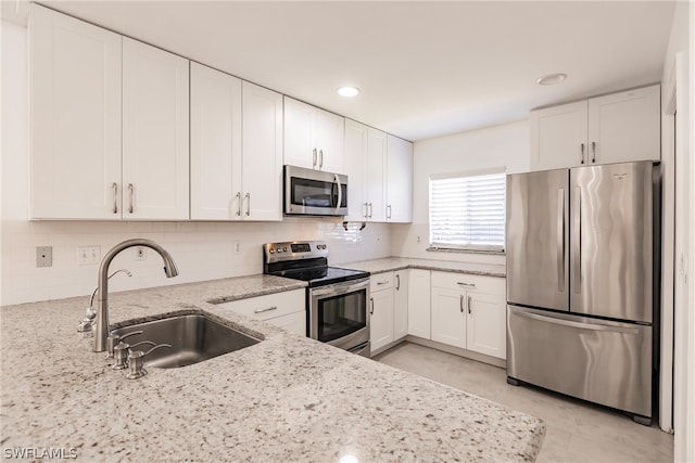 kitchen with white cabinets, backsplash, appliances with stainless steel finishes, sink, and light stone counters