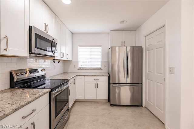 kitchen featuring white cabinetry, stainless steel appliances, light tile floors, light stone counters, and tasteful backsplash