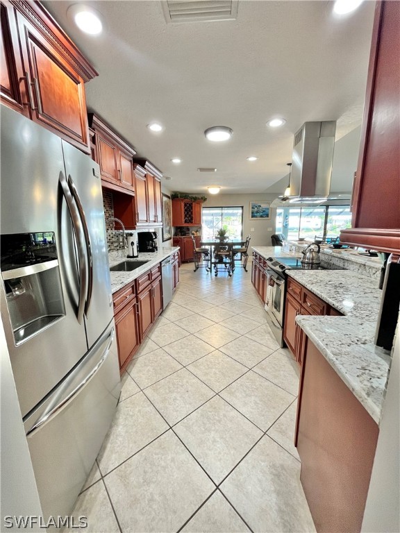 kitchen with sink, light tile patterned floors, appliances with stainless steel finishes, island range hood, and light stone counters