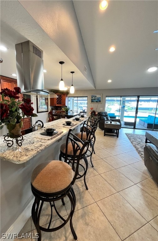 kitchen with vaulted ceiling, light stone countertops, decorative light fixtures, island range hood, and a breakfast bar area