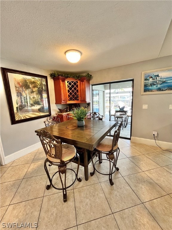 dining space featuring bar area, a textured ceiling, and light tile patterned flooring