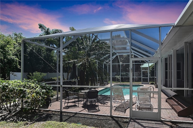 pool at dusk featuring glass enclosure and a patio