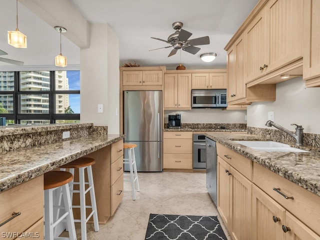 kitchen with appliances with stainless steel finishes, ceiling fan, light tile floors, sink, and a kitchen breakfast bar