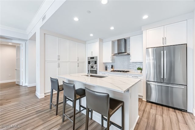 kitchen with a breakfast bar, stainless steel appliances, white cabinetry, and wall chimney range hood