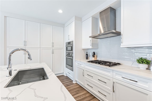 kitchen with white cabinets, hardwood / wood-style floors, sink, and wall chimney range hood