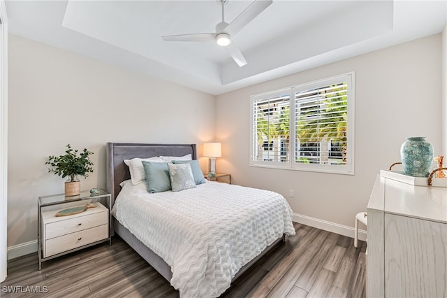 bedroom with a raised ceiling, ceiling fan, and dark hardwood / wood-style flooring