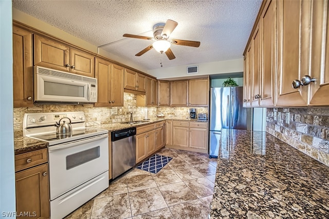 kitchen with sink, appliances with stainless steel finishes, ceiling fan, and dark stone counters