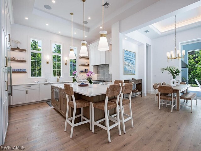 kitchen featuring white cabinets, a kitchen island, a raised ceiling, and hanging light fixtures