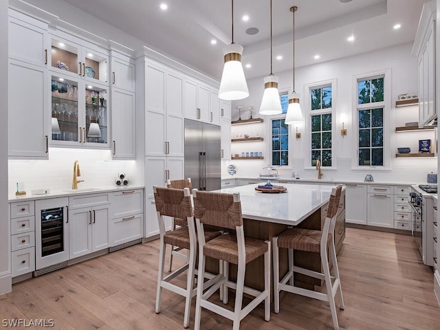 kitchen featuring sink, hanging light fixtures, beverage cooler, premium appliances, and white cabinets