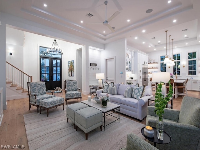 living room featuring ceiling fan with notable chandelier, a raised ceiling, light wood-type flooring, and french doors