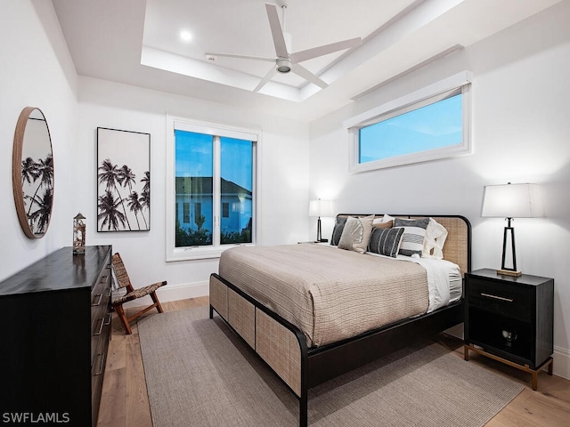 bedroom with hardwood / wood-style floors, ceiling fan, and a raised ceiling