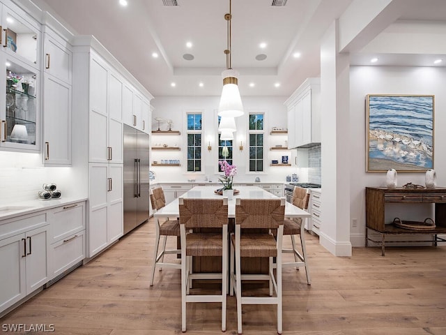 kitchen featuring pendant lighting, a breakfast bar, high end appliances, white cabinets, and a raised ceiling