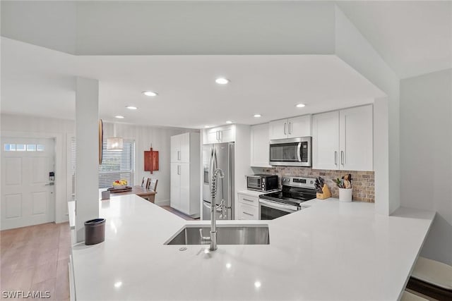 kitchen featuring appliances with stainless steel finishes, tasteful backsplash, light hardwood / wood-style floors, white cabinets, and kitchen peninsula