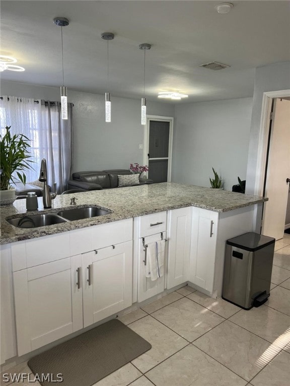 kitchen with white cabinetry, light tile flooring, light stone counters, sink, and pendant lighting