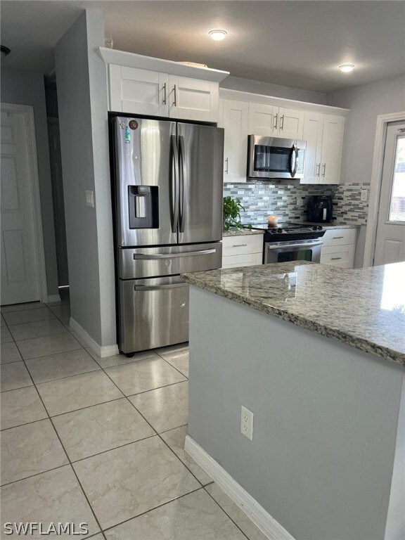 kitchen with backsplash, stainless steel appliances, white cabinets, and light tile floors